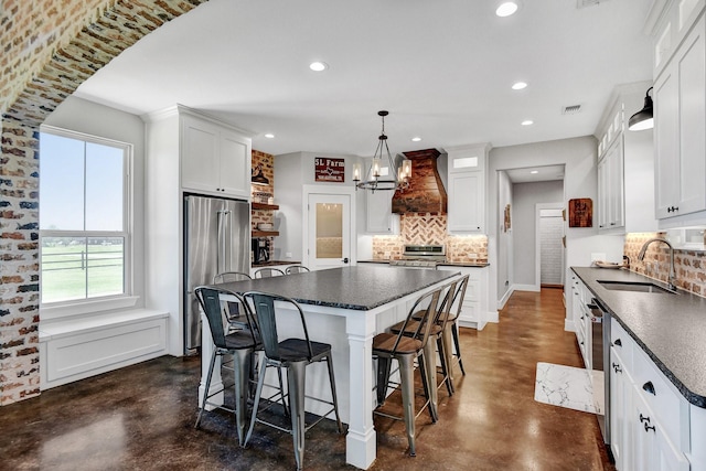 kitchen featuring finished concrete flooring, a sink, premium range hood, dark countertops, and appliances with stainless steel finishes