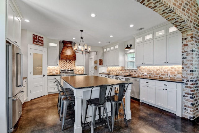 kitchen featuring a sink, stainless steel appliances, visible vents, concrete flooring, and premium range hood