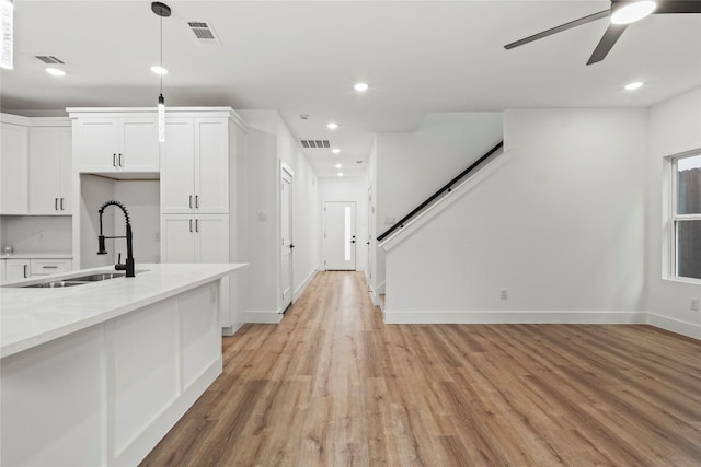 kitchen with a sink, visible vents, ceiling fan, white cabinets, and light wood-style floors