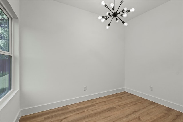 empty room featuring a chandelier, baseboards, and light wood finished floors