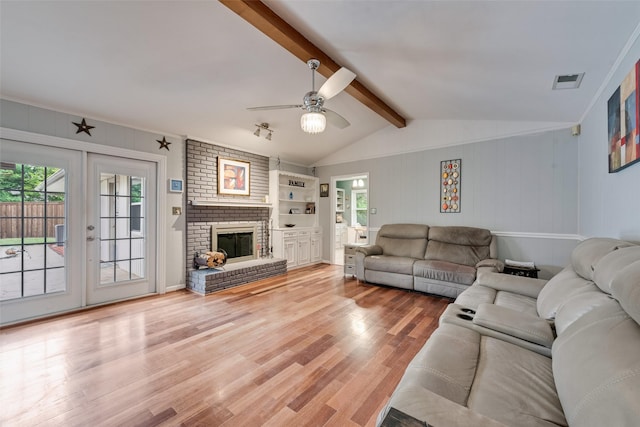 living area with ceiling fan, visible vents, a brick fireplace, light wood-type flooring, and vaulted ceiling with beams