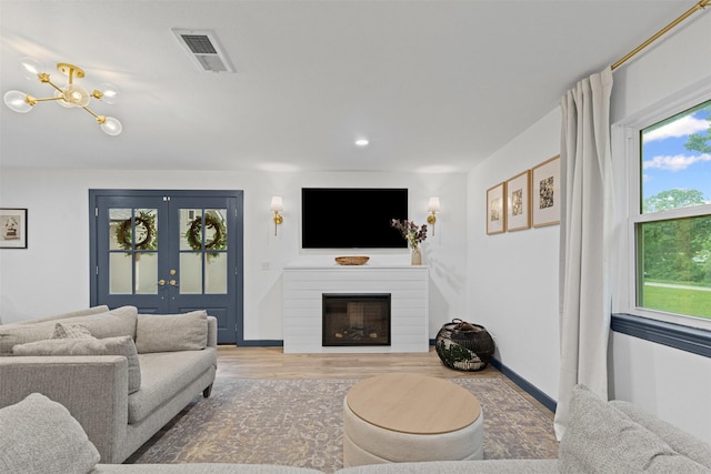 living area featuring wood finished floors, a glass covered fireplace, recessed lighting, french doors, and baseboards