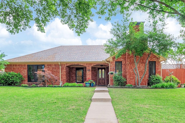 ranch-style house with fence, a shingled roof, brick siding, and a front yard