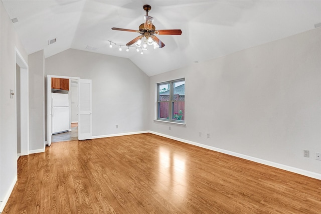 unfurnished bedroom featuring freestanding refrigerator, light wood-type flooring, visible vents, vaulted ceiling, and baseboards
