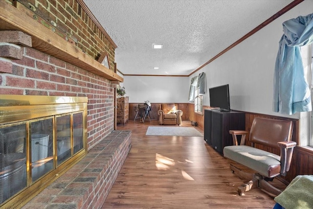 sitting room featuring wood finished floors, a textured ceiling, crown molding, a brick fireplace, and wainscoting