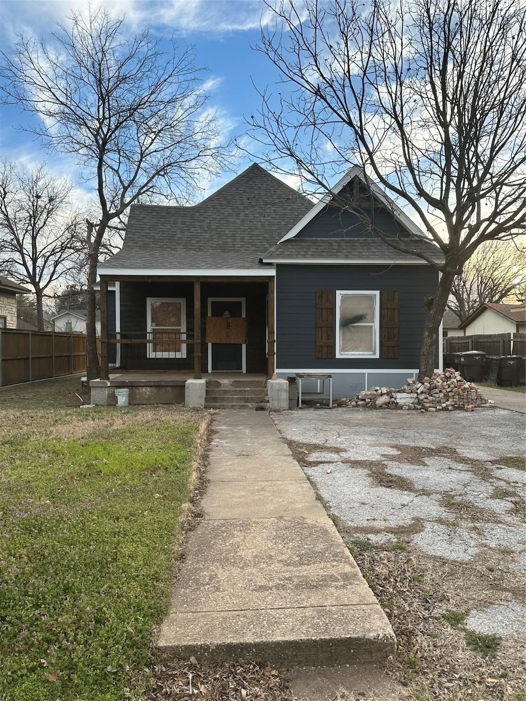 bungalow-style house featuring a porch, roof with shingles, fence, and a front yard