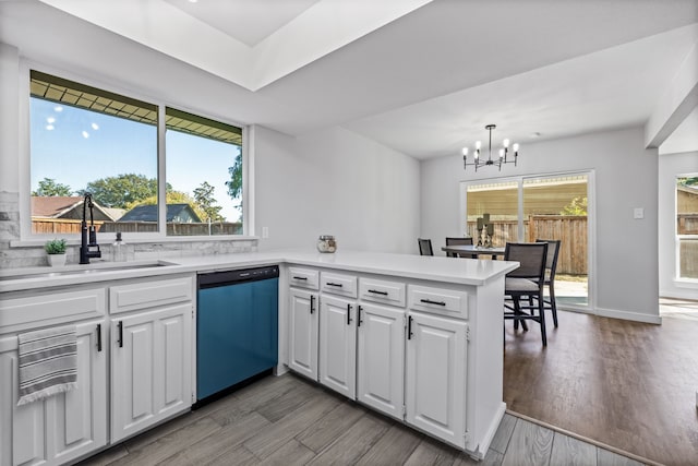 kitchen with a peninsula, dishwashing machine, a sink, light countertops, and a chandelier
