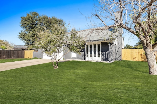 view of front of home with driveway, brick siding, a front yard, and fence