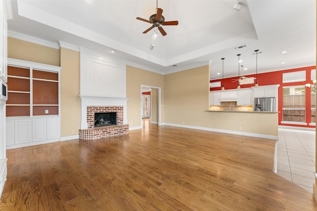 unfurnished living room with a fireplace, light wood-type flooring, a raised ceiling, ceiling fan, and recessed lighting