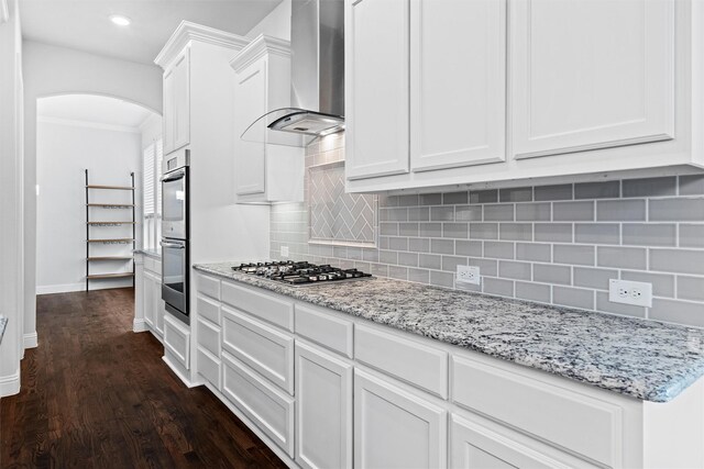 2507 Lavaca Dr, Euless, TX 76039 - kitchen with arched walkways, wall chimney exhaust hood, appliances with stainless steel finishes, dark wood-style flooring, and white cabinetry