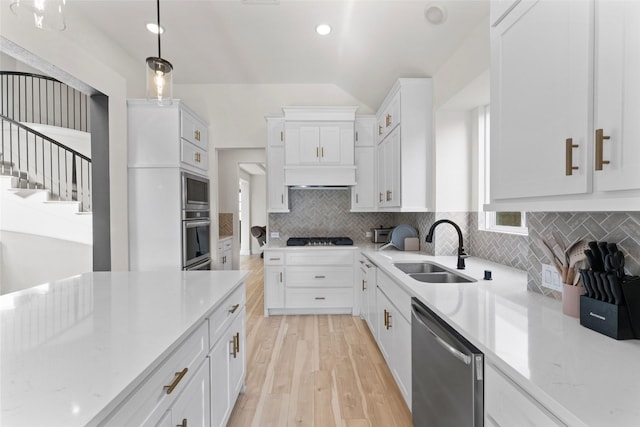 kitchen with a sink, stainless steel appliances, tasteful backsplash, light wood-type flooring, and white cabinets