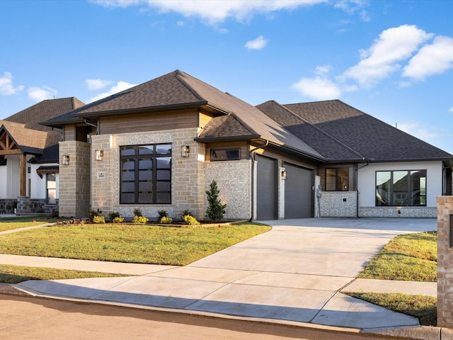 prairie-style house featuring an attached garage, stone siding, concrete driveway, a shingled roof, and a front yard