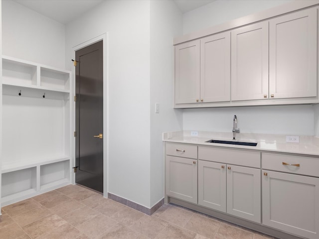 kitchen with gray cabinetry, light countertops, baseboards, and a sink