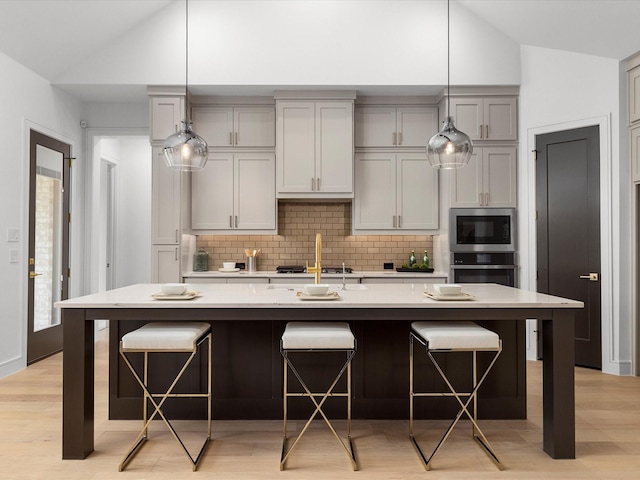 kitchen featuring appliances with stainless steel finishes, a kitchen breakfast bar, decorative backsplash, light countertops, and light wood-style floors