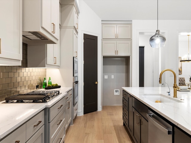 kitchen featuring pendant lighting, a sink, backsplash, light wood-style floors, and stainless steel appliances