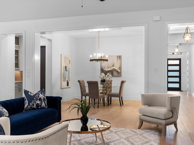 living room with light wood finished floors, ceiling fan with notable chandelier, and baseboards
