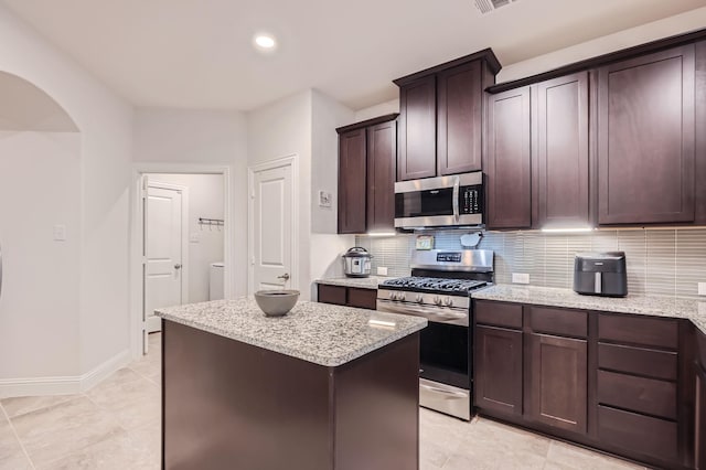 2828 Ainsworth Rd, Aubrey, TX 76227 - kitchen with appliances with stainless steel finishes, tasteful backsplash, a kitchen island, light stone counters, and dark brown cabinets