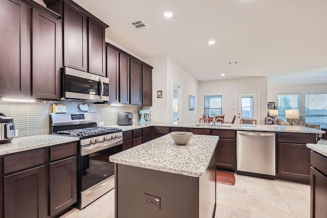 2828 Ainsworth Rd, Aubrey, TX 76227 - kitchen with stainless steel appliances, a peninsula, dark brown cabinets, a sink, and tasteful backsplash