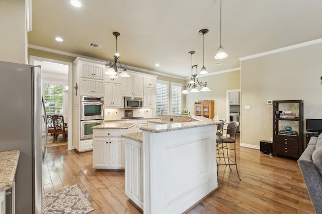 308 Dunlin Ln, Coppell, TX 75019 - kitchen featuring appliances with stainless steel finishes, a kitchen breakfast bar, crown molding, a kitchen island with sink, and light wood-type flooring