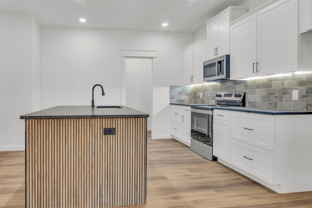 kitchen with dark countertops, appliances with stainless steel finishes, light wood-style floors, and a sink