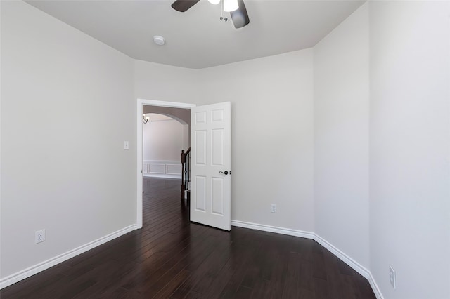 spare room featuring arched walkways, a ceiling fan, baseboards, and dark wood finished floors