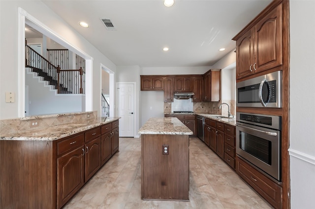 kitchen with tasteful backsplash, light stone counters, visible vents, a center island, and appliances with stainless steel finishes