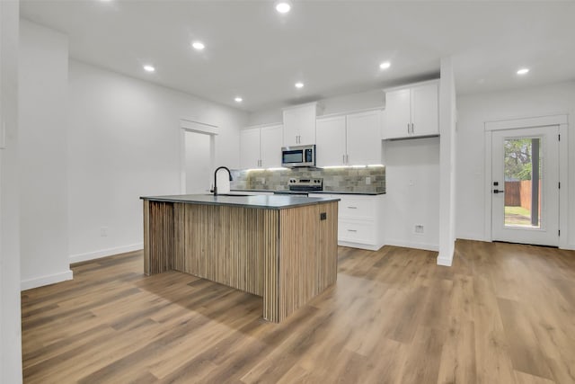 kitchen with stainless steel appliances, tasteful backsplash, light wood-style flooring, baseboards, and dark countertops