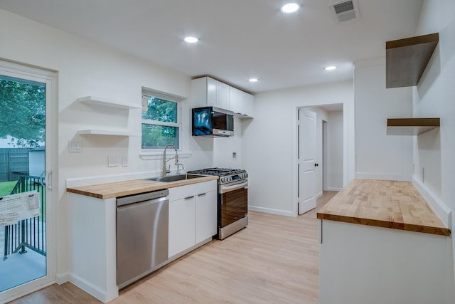 kitchen with wooden counters, a sink, open shelves, stainless steel appliances, and light wood-type flooring