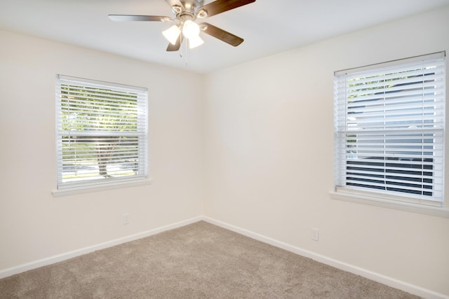 carpeted spare room featuring a wealth of natural light, baseboards, and ceiling fan