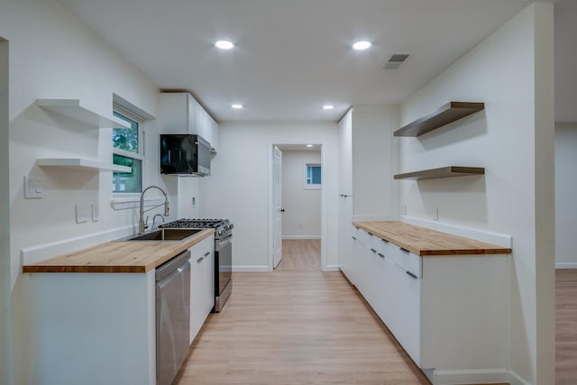 kitchen featuring a sink, wood counters, open shelves, dishwasher, and white cabinets