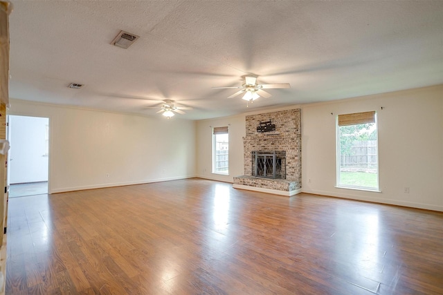 unfurnished living room with a healthy amount of sunlight, a ceiling fan, visible vents, and wood finished floors