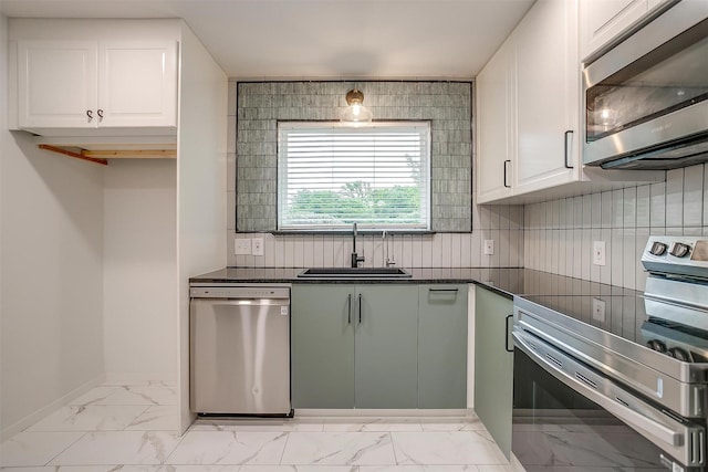 kitchen with marble finish floor, a sink, dark countertops, white cabinets, and appliances with stainless steel finishes