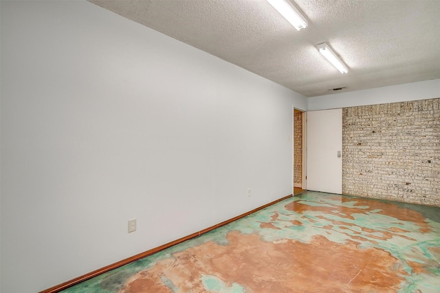 spare room with concrete flooring, a textured ceiling, visible vents, and baseboards
