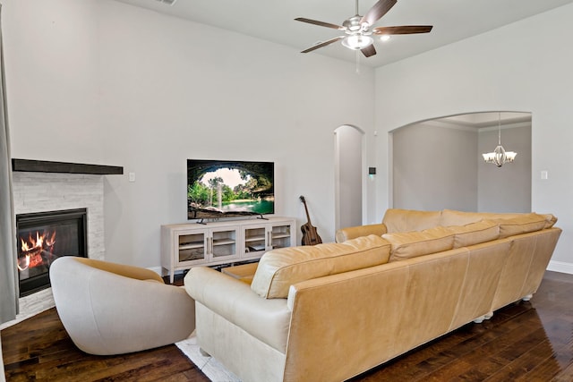 living area featuring arched walkways, a fireplace, dark wood-style floors, and ceiling fan with notable chandelier