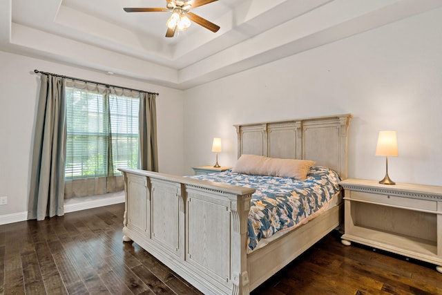 bedroom featuring a tray ceiling, dark wood-style flooring, baseboards, and ceiling fan