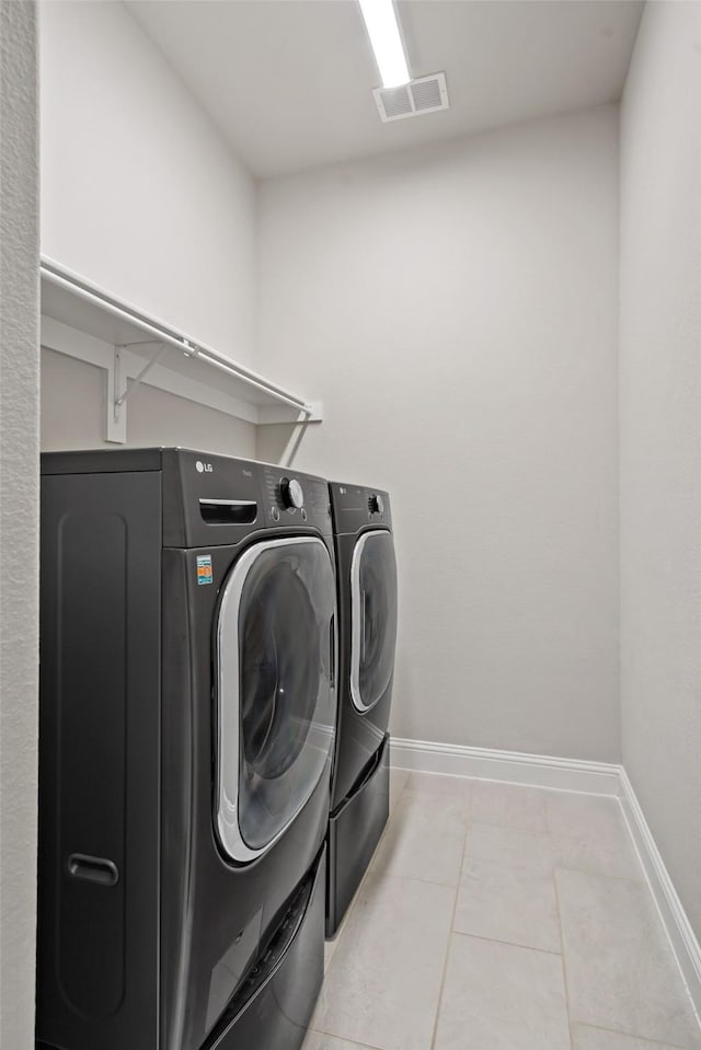 washroom with laundry area, washer and clothes dryer, visible vents, baseboards, and tile patterned flooring