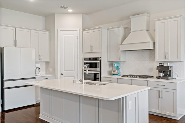 kitchen with visible vents, a sink, premium range hood, tasteful backsplash, and appliances with stainless steel finishes