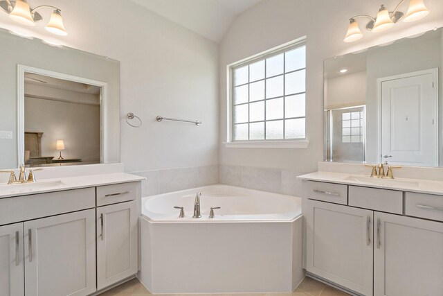 bathroom with a bath, vaulted ceiling, two vanities, and a sink