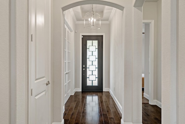 foyer entrance featuring arched walkways, ornamental molding, an inviting chandelier, and dark wood-style floors