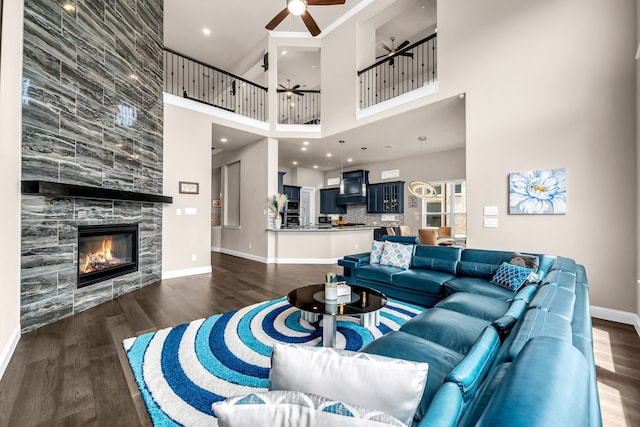 living area with ceiling fan, wood finished floors, baseboards, a fireplace, and a towering ceiling