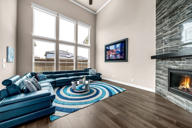 living area featuring wood finished floors, a tiled fireplace, crown molding, baseboards, and ceiling fan