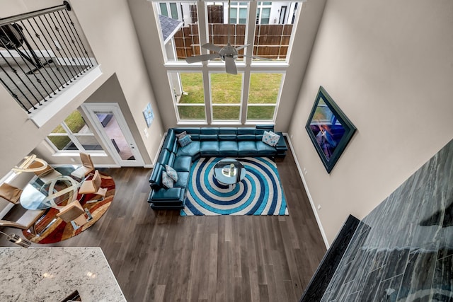 living area featuring a towering ceiling, wood finished floors, baseboards, and ceiling fan