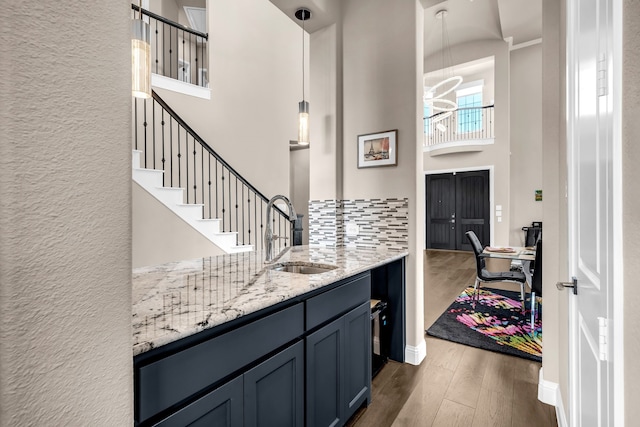 bar area featuring a sink, a towering ceiling, dark wood-type flooring, a textured wall, and decorative backsplash