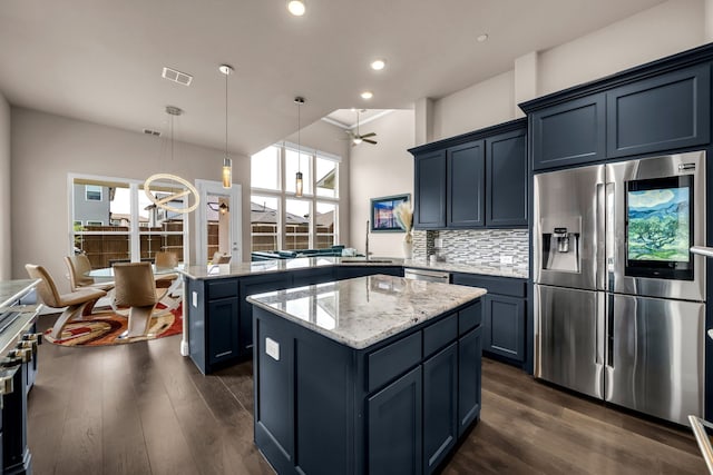 kitchen featuring appliances with stainless steel finishes, a peninsula, dark wood finished floors, light stone countertops, and plenty of natural light