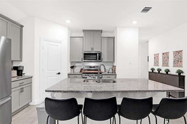 kitchen with a breakfast bar area, a sink, gray cabinets, appliances with stainless steel finishes, and light stone counters