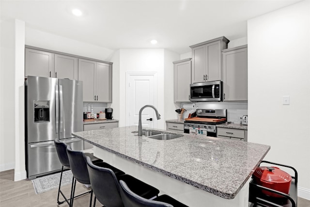 kitchen with stainless steel appliances, a kitchen breakfast bar, gray cabinetry, and a sink