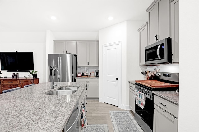 kitchen featuring a sink, light wood finished floors, gray cabinetry, and appliances with stainless steel finishes