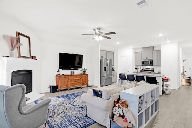 living area with a ceiling fan, recessed lighting, light wood finished floors, a glass covered fireplace, and visible vents