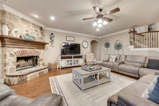 living room featuring a ceiling fan, a stone fireplace, ornamental molding, and wood finished floors