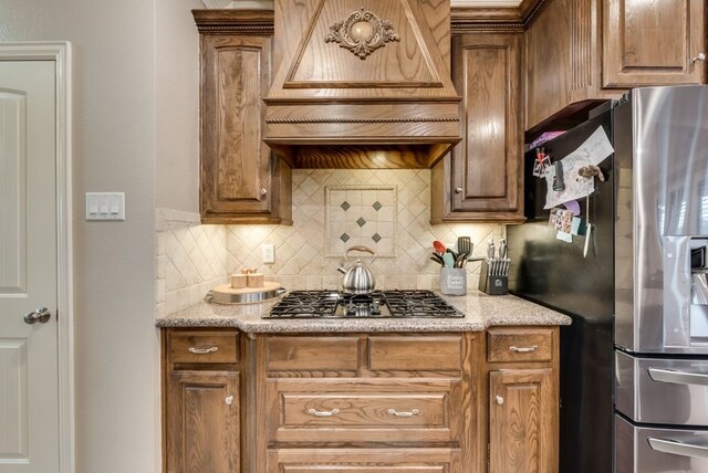 kitchen featuring custom exhaust hood, stainless steel appliances, decorative backsplash, and light stone counters